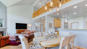 A spacious living area with a dining table, comfortable seating, a flat-screen TV, and a staircase leading to an upper level. - Golf course-front home with deck, hot tub, fireplace, W&D, & community pool (Eagle Crest)