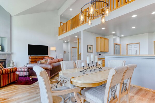 A spacious living area with a dining table, comfortable seating, a flat-screen TV, and a staircase leading to an upper level.