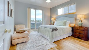 A bedroom with a bed, a chair, a nightstand, a lamp, a ceiling fan, and a view through a window. - Golf course-front home with deck, hot tub, fireplace, W&D, & community pool (Eagle Crest)