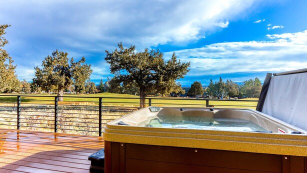 A hot tub on a wooden deck with a view of a golf course and trees. - Golf course-front home with deck, hot tub, fireplace, W&D, & community pool (Eagle Crest)