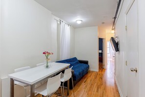 Ein kleiner, kompakter Raum mit einem weißen Tisch, zwei weißen Stühlen, einem blauen Sofa und einem Holzboden.