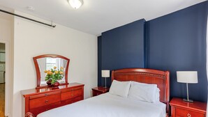 A hotel room with a large bed, wooden headboard, two bedside tables with lamps, a dresser, and a mirror.