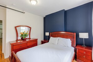 A hotel room with a large bed, wooden headboard, two bedside tables with lamps, a dresser, and a mirror.