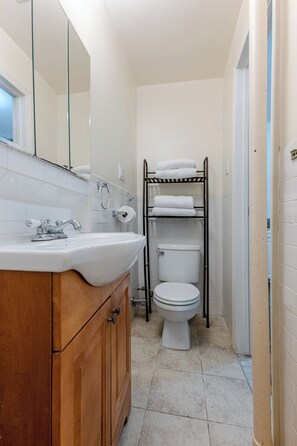 A bathroom with a wooden vanity, a white sink, a mirror, a toilet, and a towel rack.
