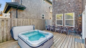 Een hottub op een houten terras, een houten hek en een gebouw met ramen.