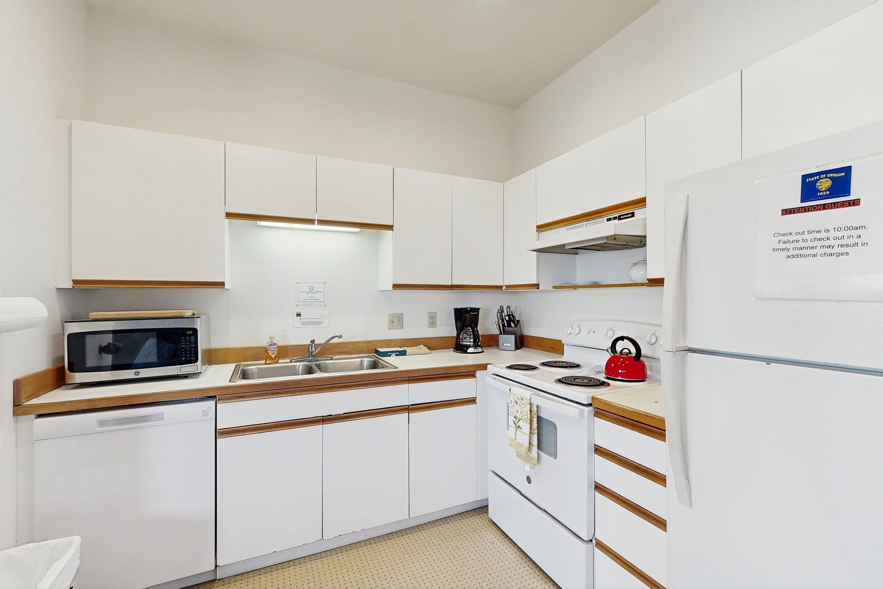 Una cocina con armarios blancos, microondas, cafetera, hervidor y refrigerador.