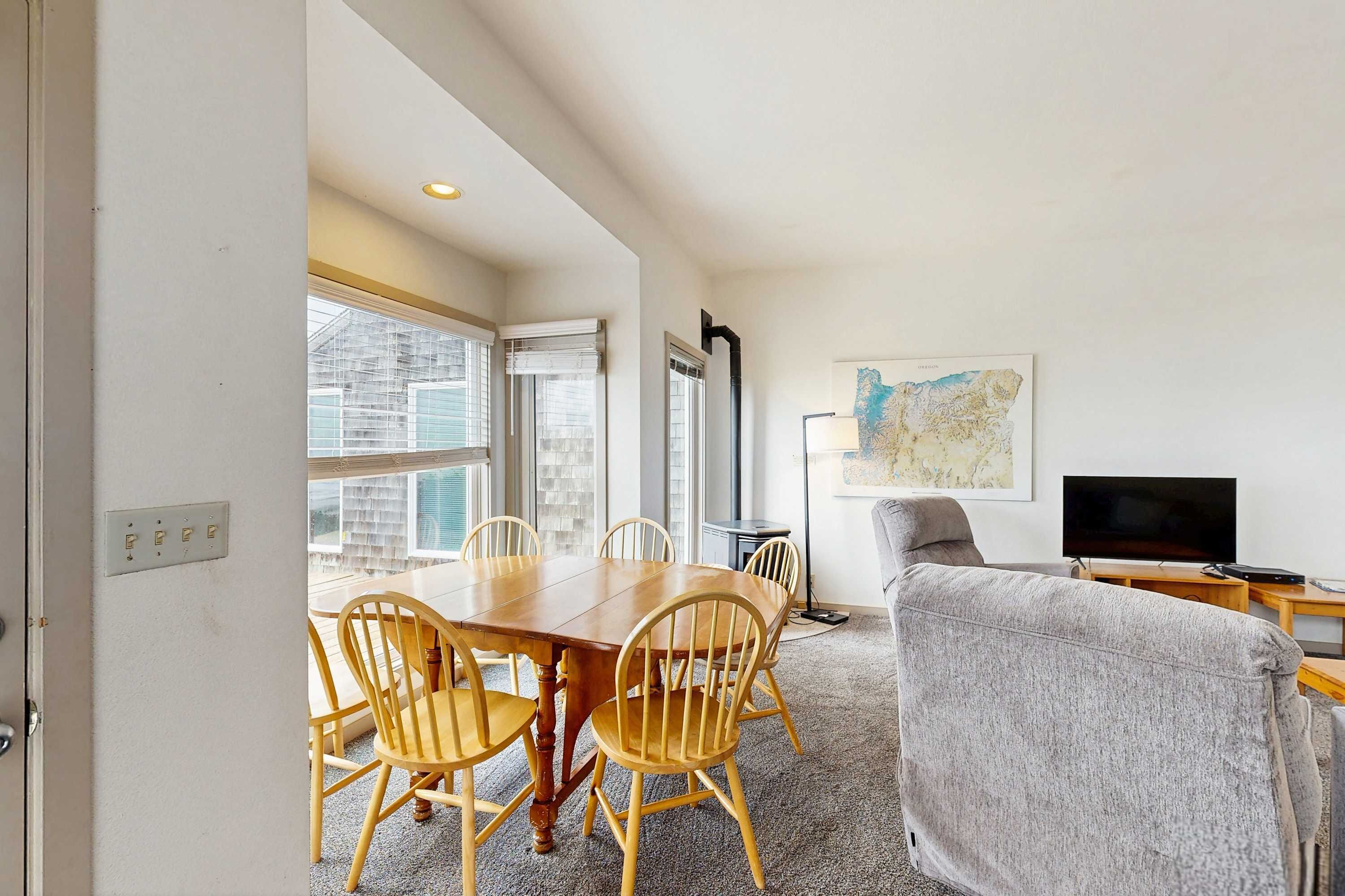 A room with a dining table, chairs, a grey sofa, a TV, and a map on the wall.