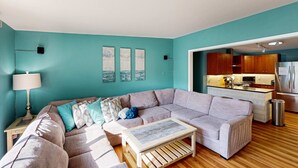 Ein Wohnzimmer mit einer Eckcouch, einem Couchtisch und einem durch eine offene Tür einsehbaren Küchenbereich.