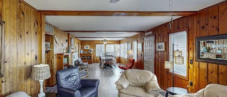 A wooden-paneled room with a dining area, two sofas, a ceiling fan, and a fireplace.