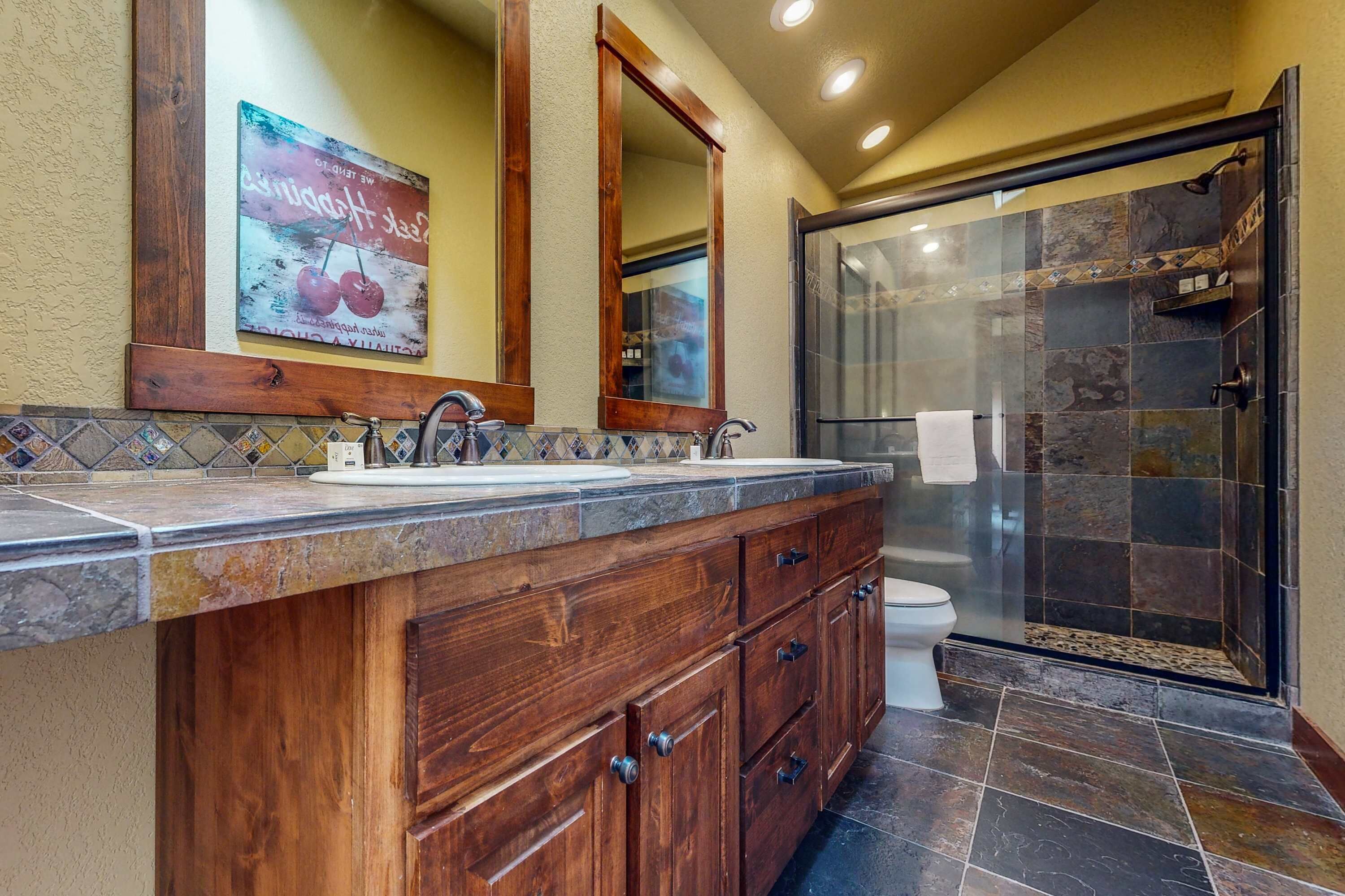 Une salle de bain avec un meuble-lavabo en bois, deux vasques, des toilettes et une douche à parois de verre.