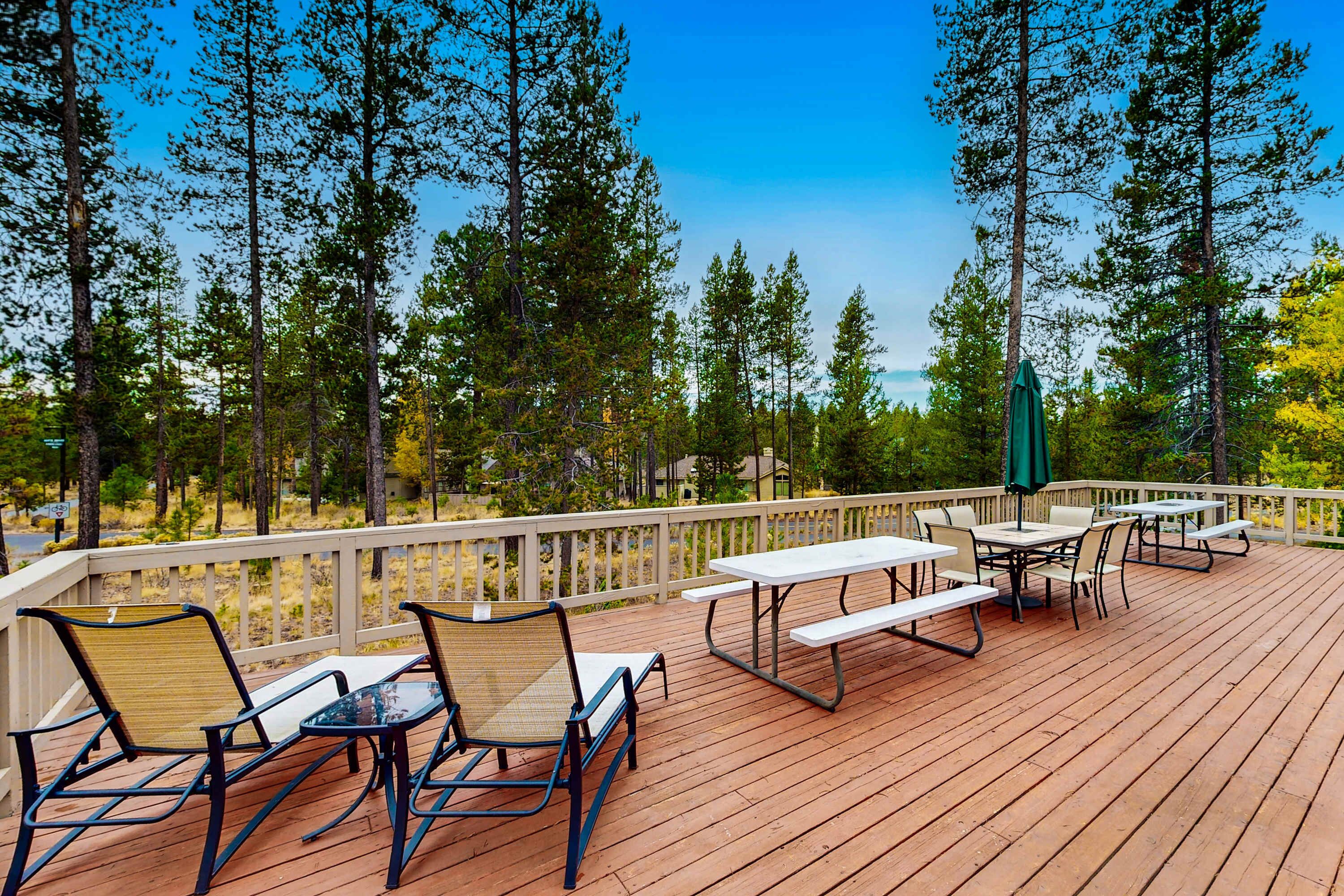 A wooden deck with outdoor furniture, surrounded by trees and a clear sky.
