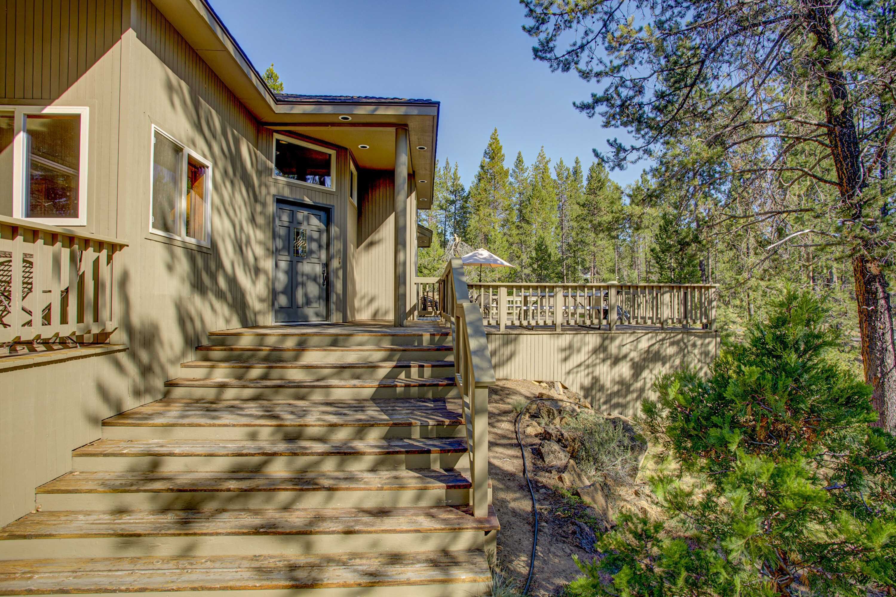 A wooden staircase leading to a front door, surrounded by a wooden fence and trees.