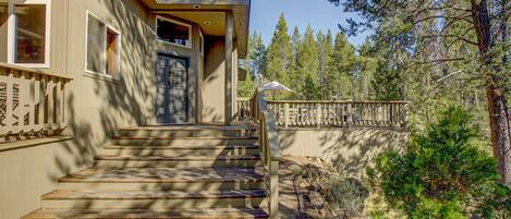 A wooden staircase leading to a front door, surrounded by a wooden fence and trees.