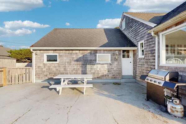 Ein Haus mit überdachter Terrasse, Grill und weißem Picknicktisch.