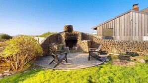 A stone oven with two chairs in front, a wooden building, and a stone wall.
