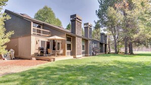 A two-story house with a covered patio, a chimney, and a well-maintained lawn. - Open & modern condo with pool, hot tub, fireplace & W&D (Sunriver)
