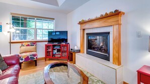 A living room with a fireplace, a television, a red sofa, and a colorful chair. - Dog-Friendly, Coastal Escape with Private Hot Tub, WiFi, & Deck - Blocks to Park (Seaside)
