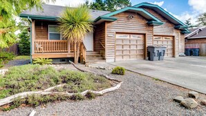 A wooden house with a garage, a front porch, and a small garden area. - Dog-Friendly, Coastal Escape with Private Hot Tub, WiFi, & Deck - Blocks to Park (Seaside)