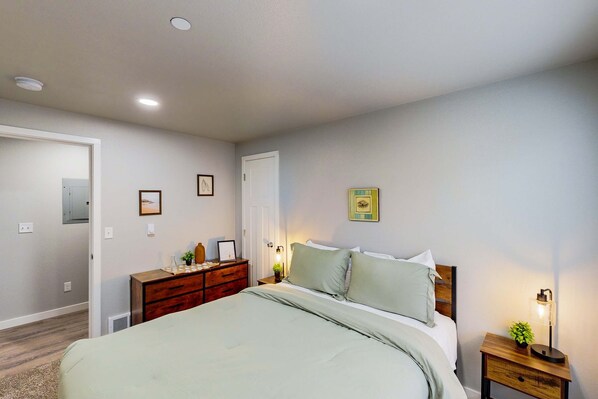 Une chambre à coucher comprenant un lit, une commode, une table de chevet et une lampe fixée au mur.