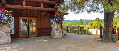 A rustic lodge with stone pillars, wooden doors, and a stone staircase leading to the entrance.