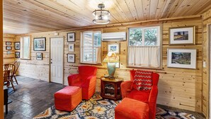 A wooden interior with a ceiling fan, framed pictures, a red sofa, and a patterned rug.