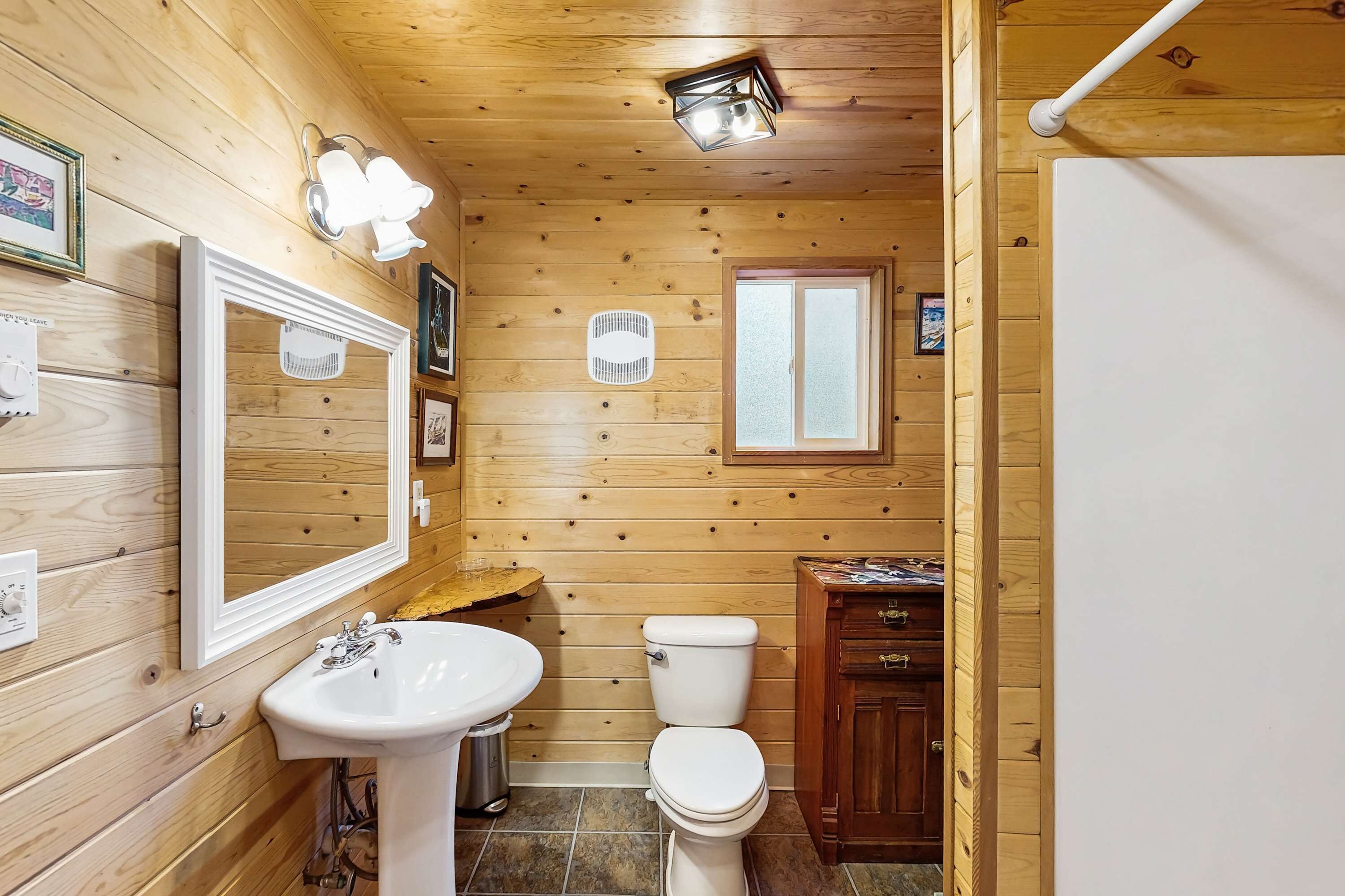Et badeværelse med træpaneler, vask, toilet og skab.