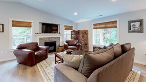 A living room with a fireplace, leather chairs, a sofa, and a bookshelf. - Brand-new home with hot tub, deck, fast WiFi, central AC, & great location (Manzanita)
