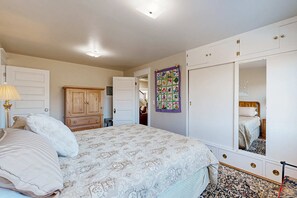 A bedroom with a bed, a wardrobe, a mirror, and a wall hanging.