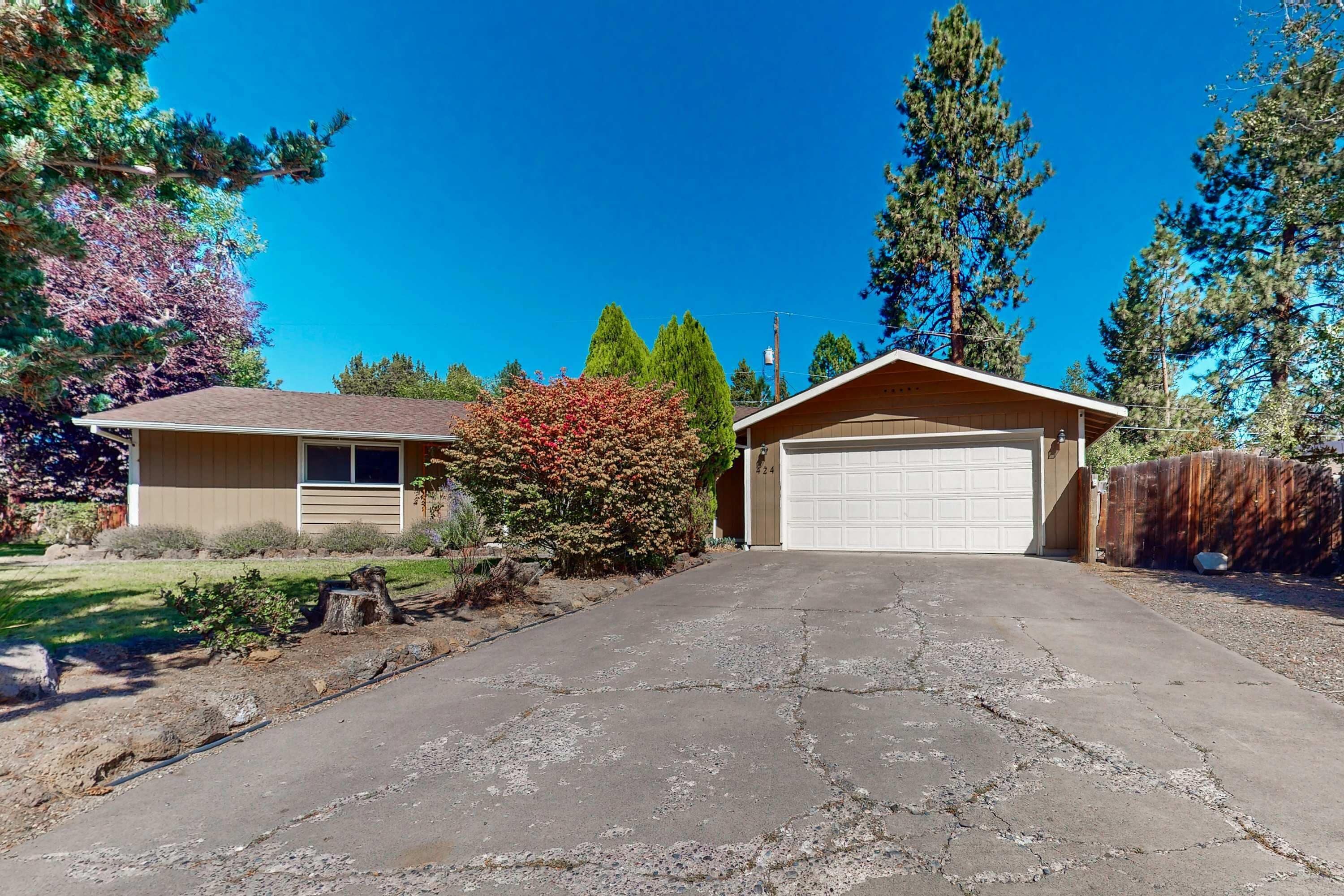 A residential property with a garage, driveway, and surrounding trees.