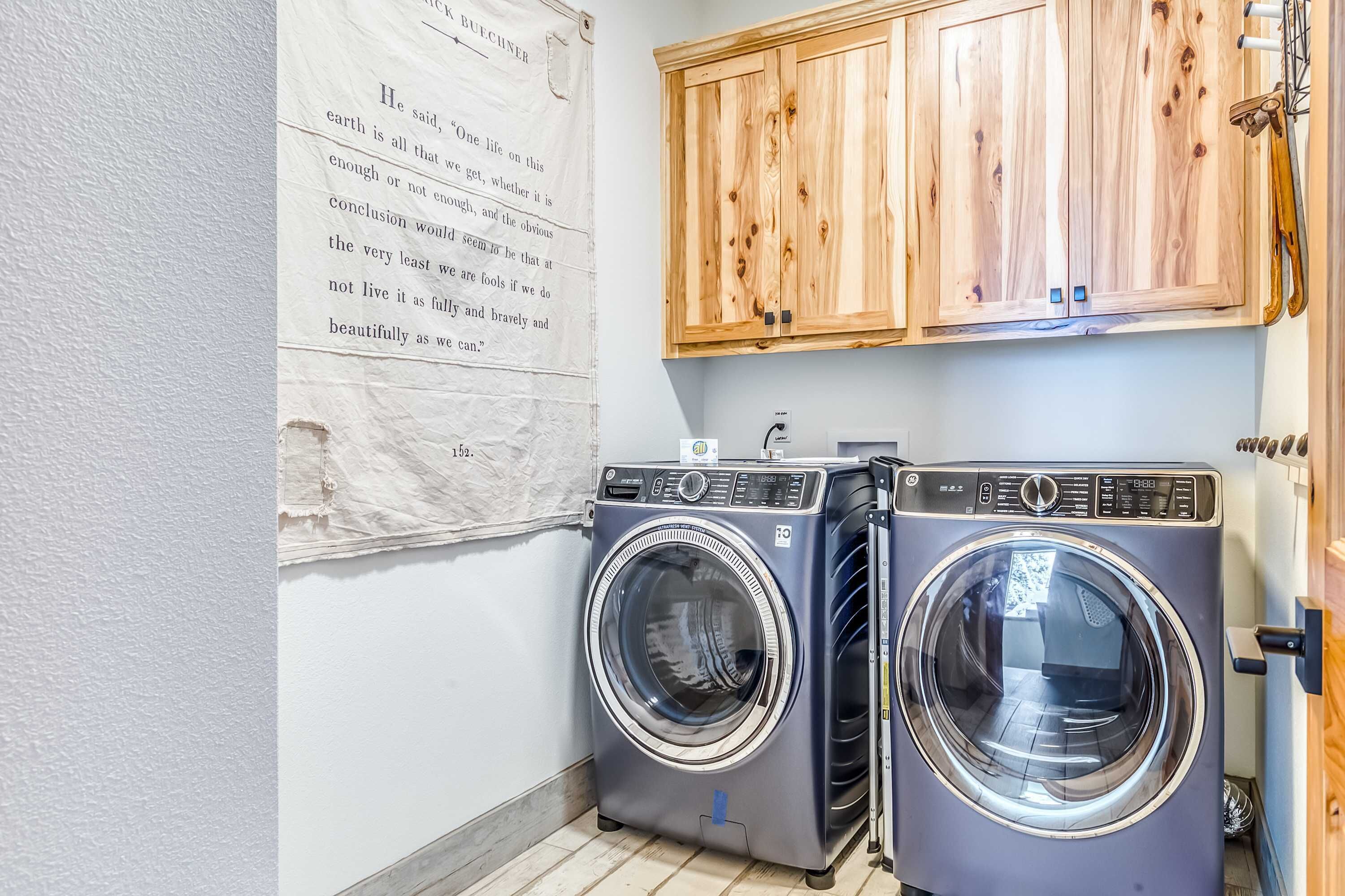 A laundry room with two front-loading washing machines, wooden cabinets above, and a wall-mounted sign.