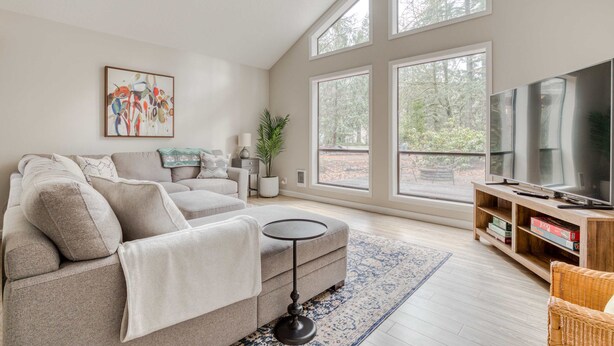 A living room with a sofa, a round coffee table, a television, and large windows. - Spacious Mountain Home with Decks, Firepit, Grill, Wood Stove, W&D, & Free WiFi (Rhododendron)