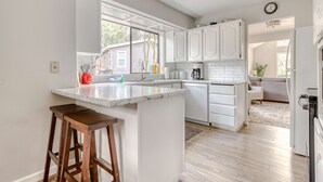 A kitchen with white cabinets, a marble countertop, wooden stools, and a view to the outside. - Spacious Mountain Home with Decks, Firepit, Grill, Wood Stove, W&D, & Free WiFi (Rhododendron)