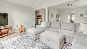 A living room with a sectional sofa, a television, a small table, and a patterned rug. - Spacious Mountain Home with Decks, Firepit, Grill, Wood Stove, W&D, & Free WiFi (Rhododendron)
