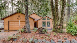 A cabin with a garage, a small porch, and a forested backdrop. - Spacious Mountain Home with Decks, Firepit, Grill, Wood Stove, W&D, & Free WiFi (Rhododendron)