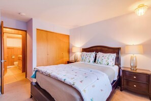 Ein Schlafzimmer mit einem Bett, Nachttischen, einem Holzschrank und einer Tür zu einem Badezimmer.