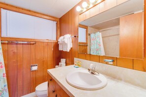 Ein Badezimmer mit Holzwänden, einem weißen Waschbecken, einem Spiegel und einer Duschvorhang.