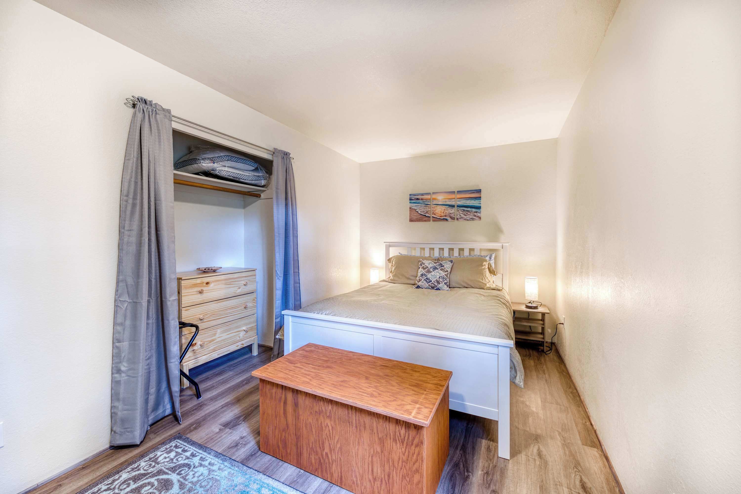A bedroom with a bed, bedside table, nightstand, wooden dresser, and a small wooden bench.
