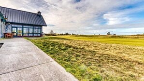 A modern building with large windows, a concrete pathway, and a grassy field in the background. - Single-level, dog-friendly home w/ private fenced-in yard & easy beach access (Bandon)