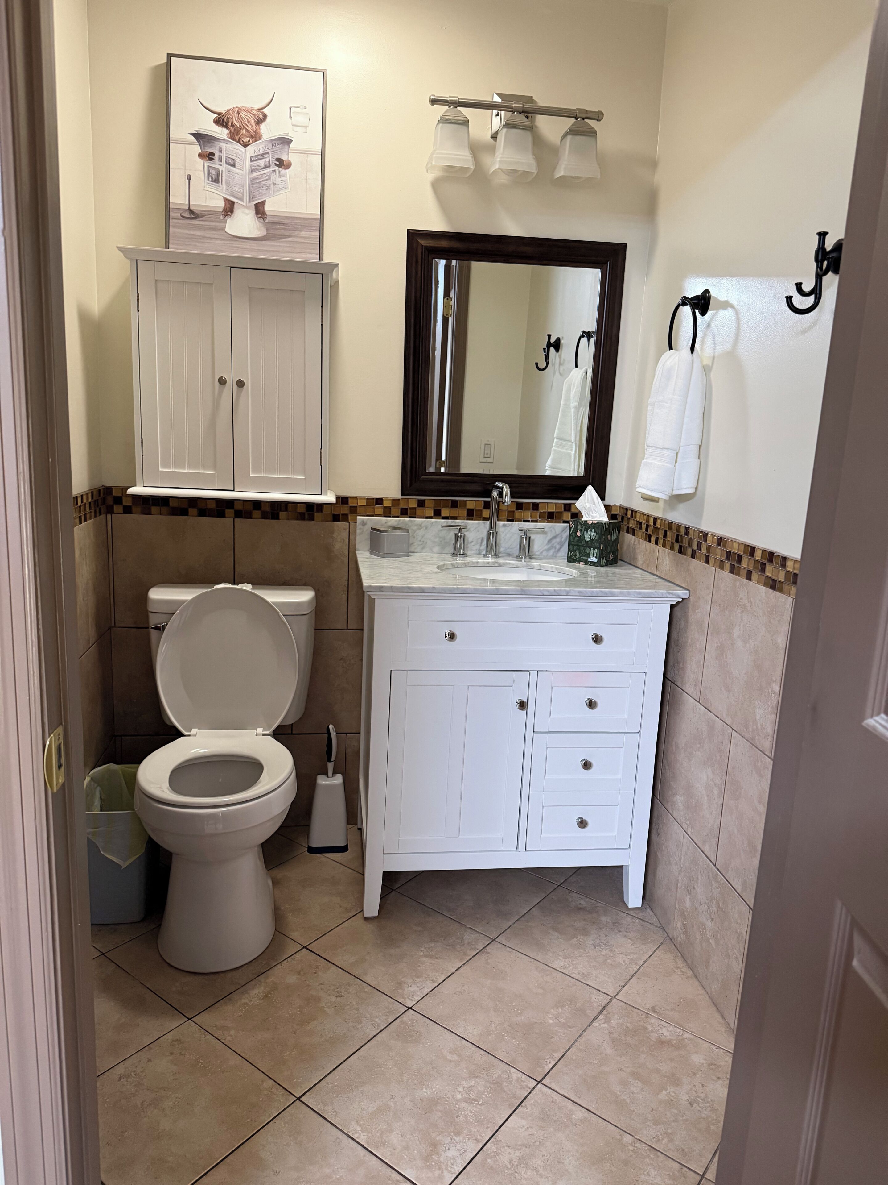 Une salle de bain comprenant des toilettes, un lavabo, un miroir, un porte-serviettes et un meuble de rangement.