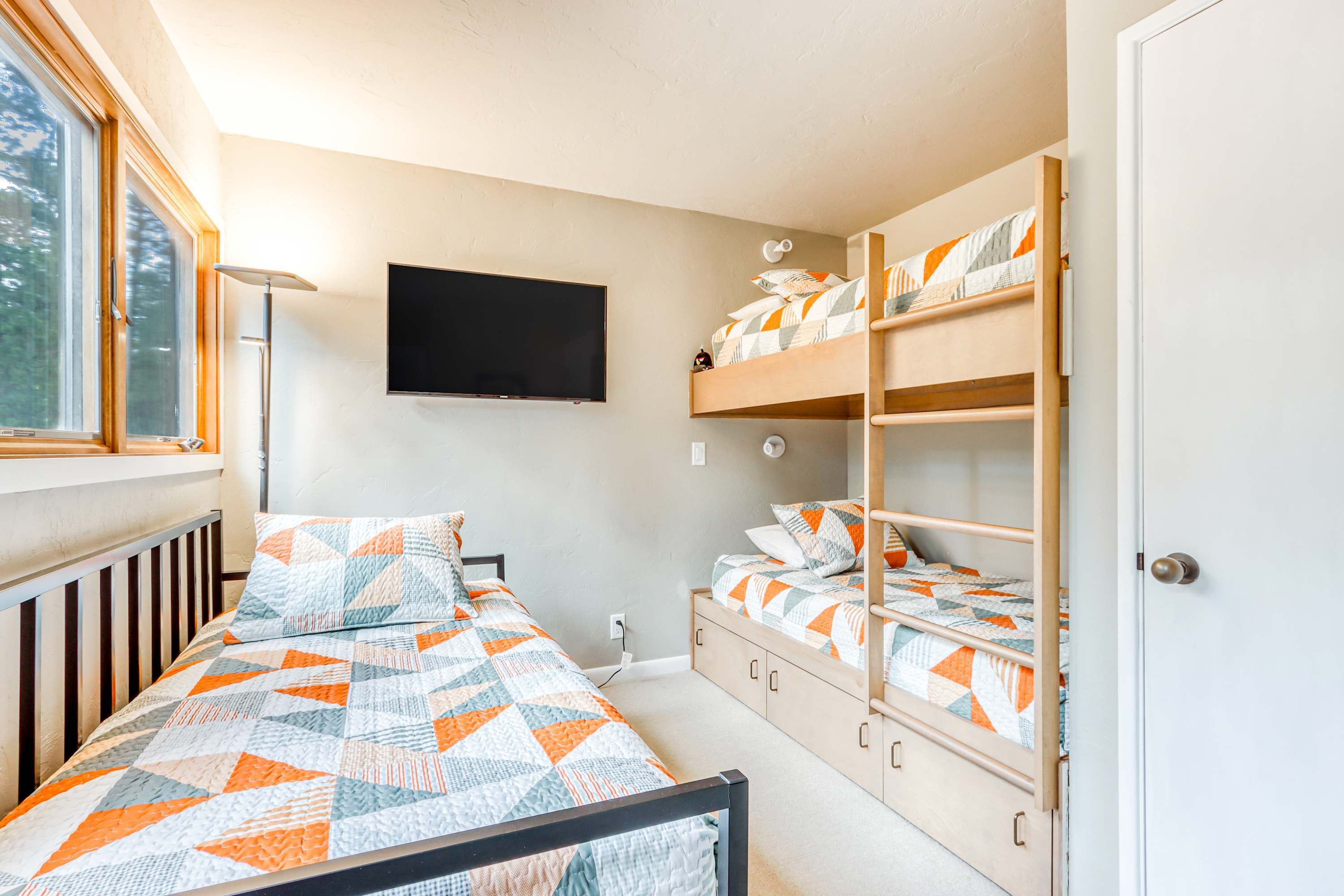Ein Schlafzimmer mit einem Einzelbett, einem Etagenbett, einem an der Wand befestigten Fernseher und einem Fenster.