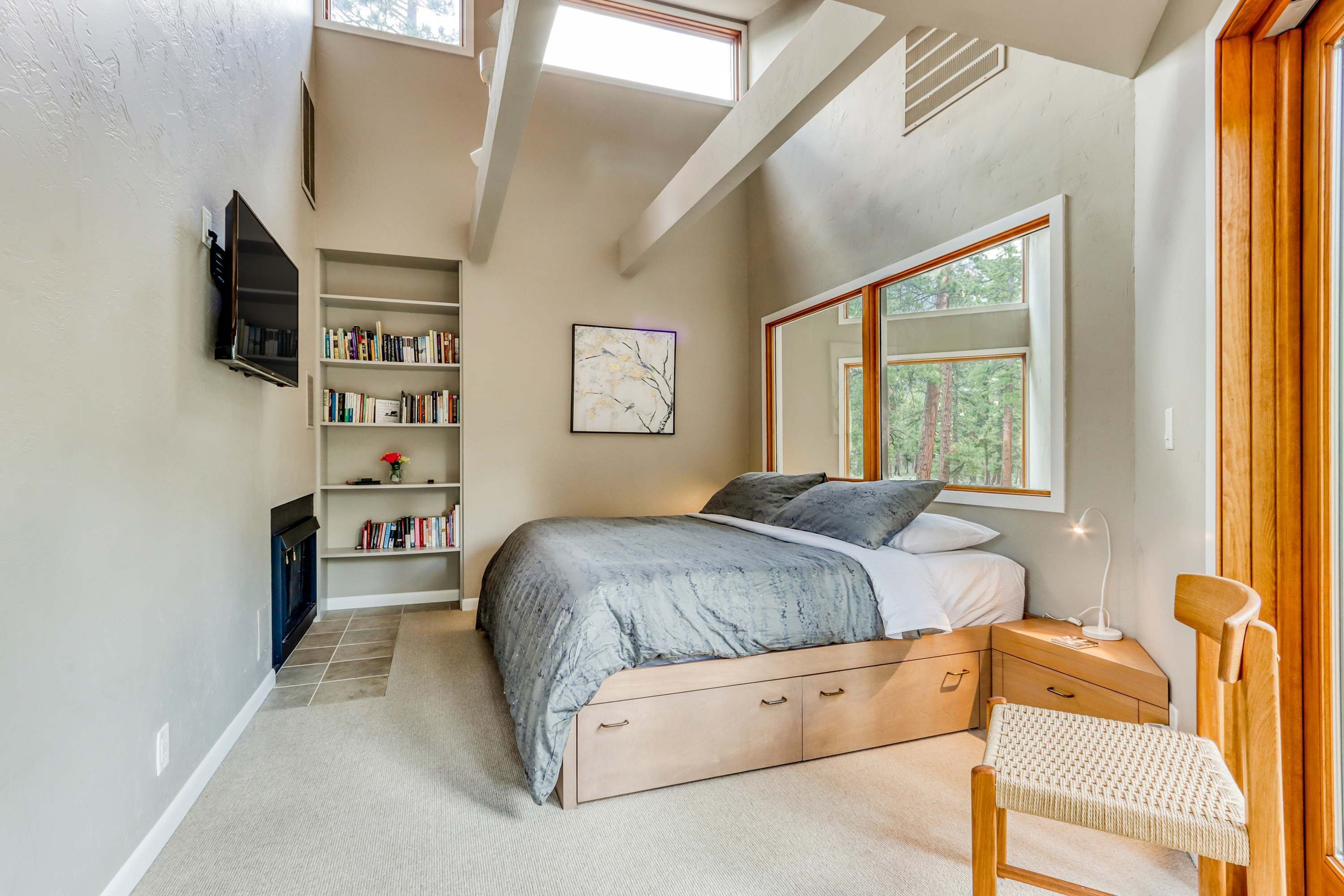 A bedroom with a bed, bedside tables, a bookshelf, a TV, and a window with a view of trees.