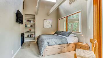 A bedroom with a bed, bedside tables, a bookshelf, a TV, and a window with a view of trees.