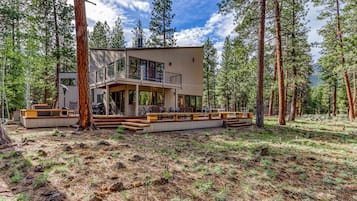 A modern two-story house surrounded by tall pine trees.