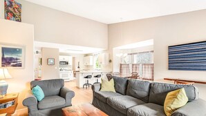 Ein Wohnzimmer mit grauem Sofa, einem Holztisch und einer Küche im Hintergrund.