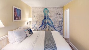 A hotel room with a bed, a brick wall mural, a painting on the wall, and a door. - Retro getaway near beach with fast WiFI - walk to downtown shops & eateries (Bandon)