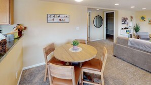 Un coin repas avec une table ronde en bois et des chaises, une petite plante en pot et un tableau représentant des oiseaux accroché au mur.