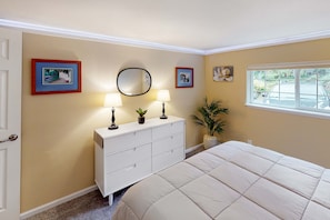 A bedroom with a bed, a dresser with lamps, a mirror, and framed pictures on the wall.