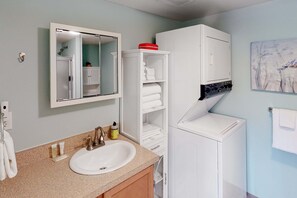 Un baño con lavamanos, espejo, armarios blancos y un perchero para toallas.