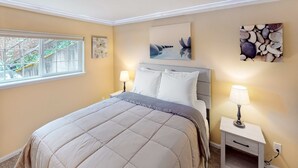 Une chambre à coucher avec un lit, deux tables de chevet avec des lampes, une fenêtre et des œuvres d’art murales.