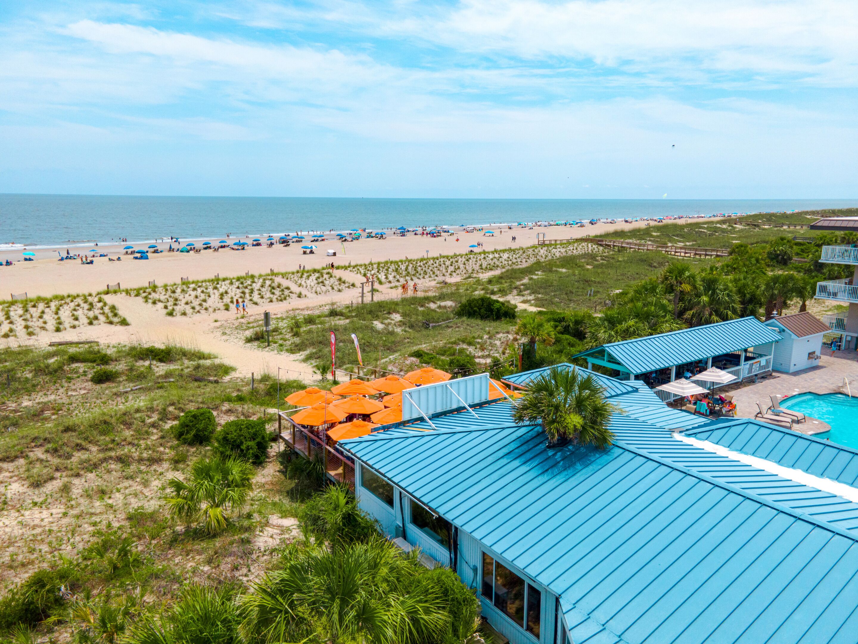 A beach resort with a swimming pool, beach umbrellas, and a view of the ocean.
